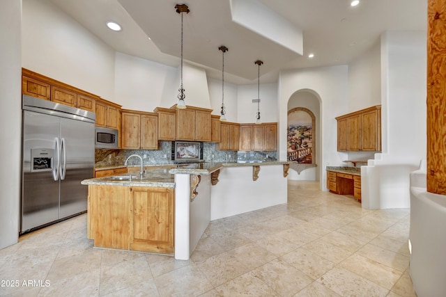 kitchen with an island with sink, a towering ceiling, built in appliances, and decorative light fixtures