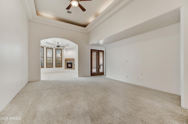 carpeted empty room featuring ceiling fan, a fireplace, a tray ceiling, and a towering ceiling