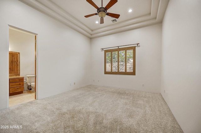 spare room featuring a raised ceiling, light colored carpet, and ceiling fan