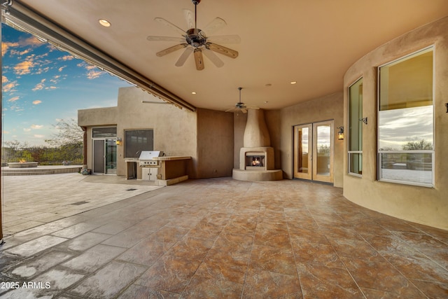 patio terrace at dusk featuring ceiling fan and a fireplace