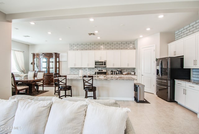 kitchen featuring light stone counters, stainless steel appliances, a breakfast bar area, and a center island with sink