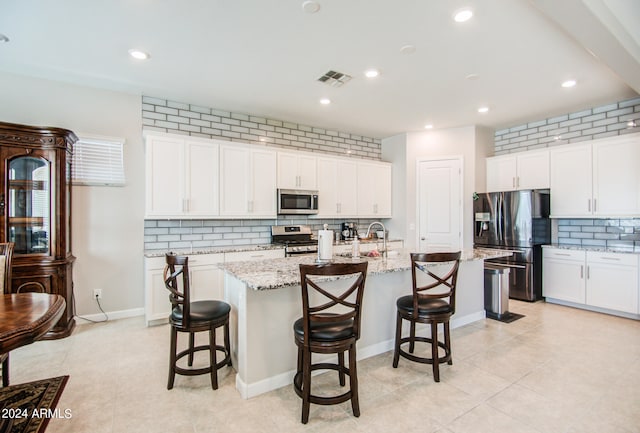 kitchen featuring tasteful backsplash, stainless steel appliances, white cabinets, a breakfast bar area, and a kitchen island with sink