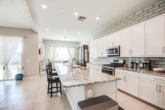 kitchen with light stone countertops, an island with sink, a kitchen breakfast bar, stainless steel appliances, and white cabinets