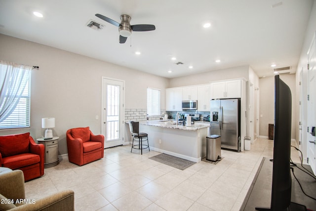 kitchen with light stone countertops, appliances with stainless steel finishes, a kitchen bar, a kitchen island, and white cabinets