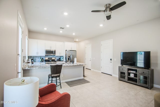 kitchen with a kitchen breakfast bar, stainless steel appliances, light stone countertops, white cabinetry, and tasteful backsplash