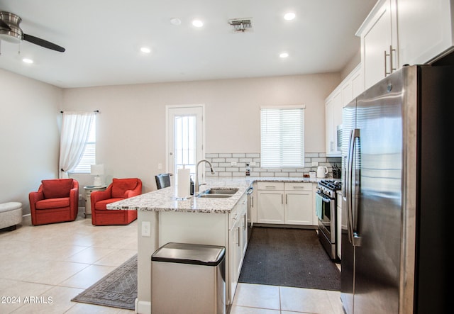 kitchen featuring decorative backsplash, kitchen peninsula, white cabinets, light tile patterned floors, and appliances with stainless steel finishes