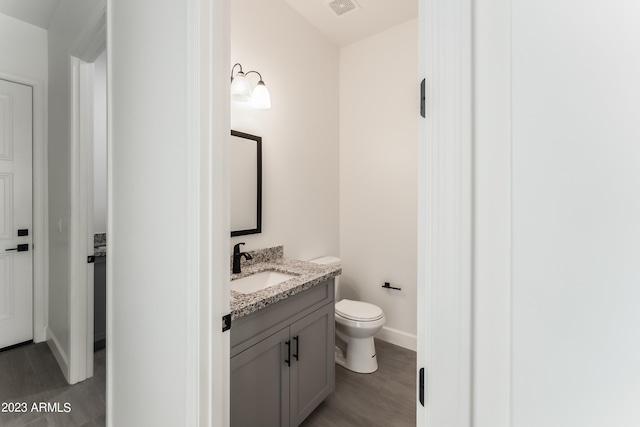 bathroom featuring vanity, toilet, baseboards, wood finished floors, and visible vents