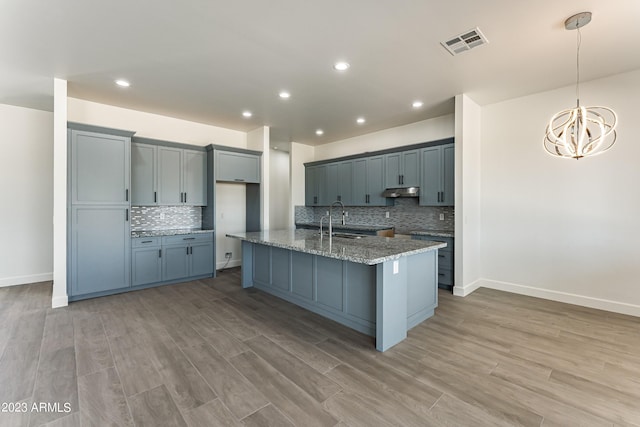 kitchen featuring decorative backsplash, visible vents, light stone countertops, a sink, and a chandelier