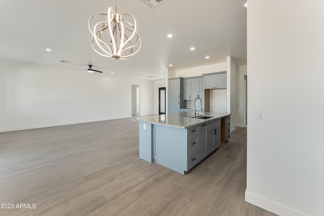kitchen featuring light stone countertops, a sink, gray cabinets, recessed lighting, and baseboards
