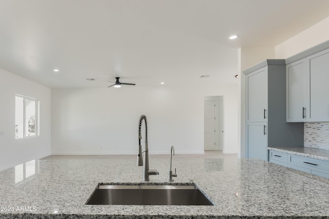 kitchen with a ceiling fan, open floor plan, light stone counters, and a sink