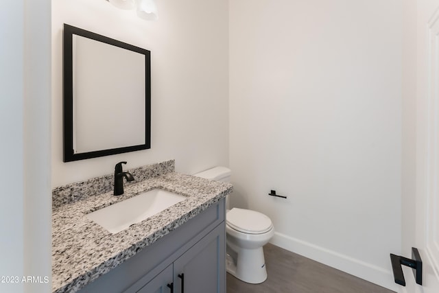 bathroom with baseboards, wood finished floors, toilet, and vanity