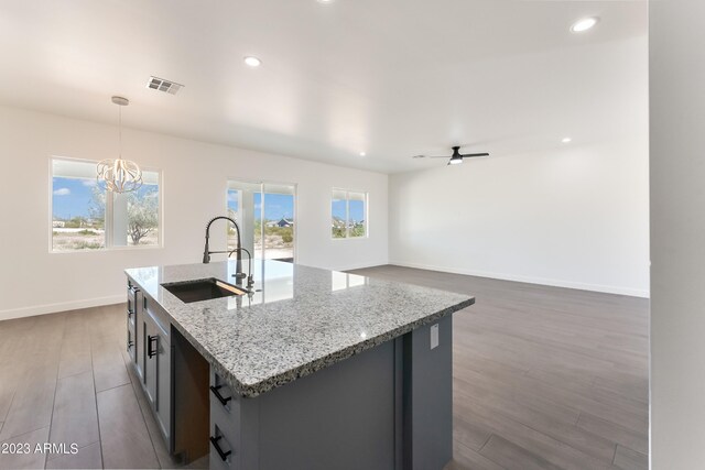 kitchen with visible vents, wood finished floors, a sink, ceiling fan with notable chandelier, and hanging light fixtures