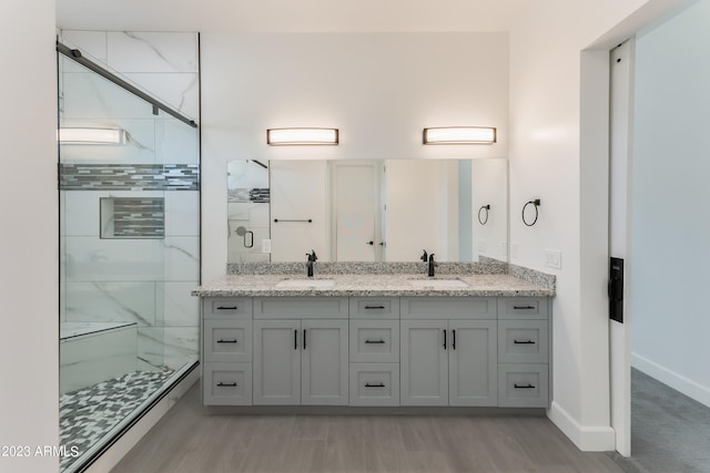 bathroom featuring double vanity, a shower stall, a sink, and wood finished floors