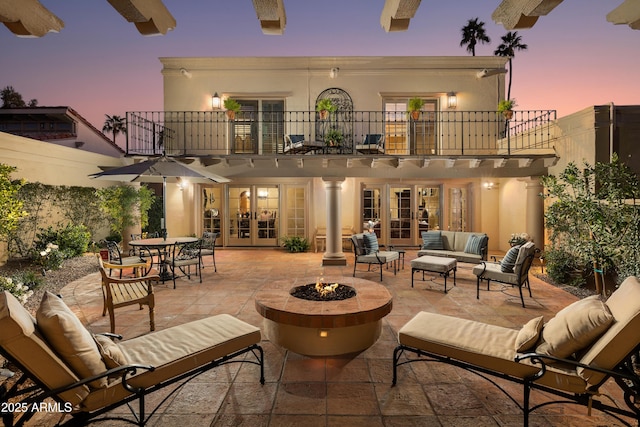 patio terrace at dusk featuring an outdoor living space with a fire pit, french doors, and a balcony