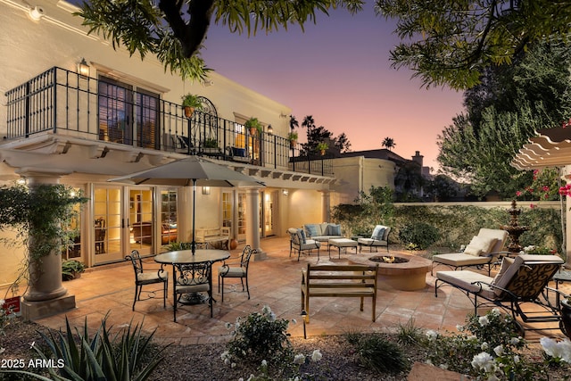 patio terrace at dusk featuring a balcony and an outdoor living space with a fire pit