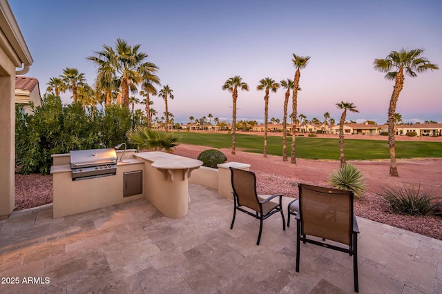 patio terrace at dusk with grilling area, exterior kitchen, and a lawn