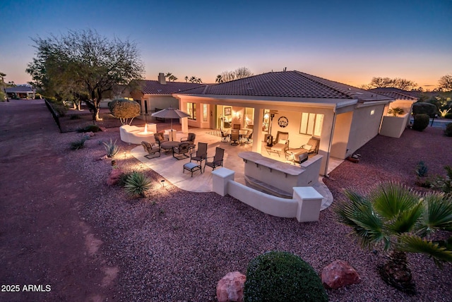 back house at dusk featuring a patio and a fire pit