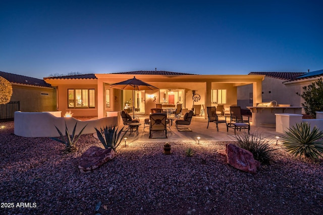 back house at dusk with an outdoor kitchen and a patio