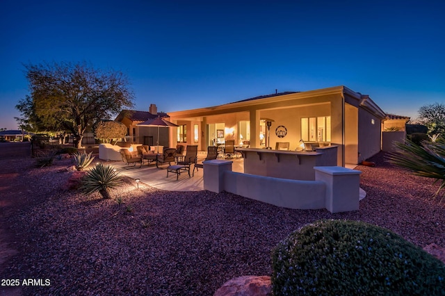 back house at dusk with a patio, outdoor lounge area, and an outdoor bar