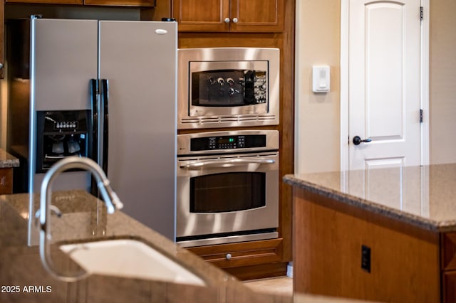 kitchen with stainless steel appliances, light stone countertops, and sink