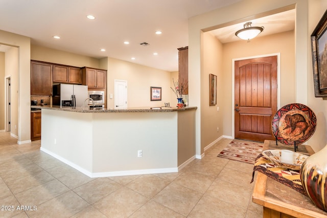 kitchen featuring appliances with stainless steel finishes, stone countertops, sink, light tile patterned floors, and kitchen peninsula