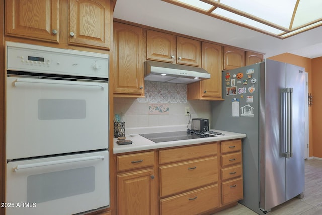 kitchen with light wood-type flooring, backsplash, double oven, stainless steel refrigerator, and black stovetop