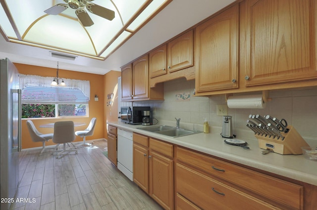 kitchen with decorative backsplash, stainless steel fridge, white dishwasher, sink, and hanging light fixtures