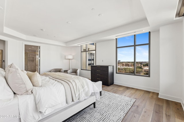 bedroom featuring light wood-style flooring, baseboards, a raised ceiling, and ensuite bathroom