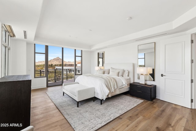 bedroom featuring access to exterior, a raised ceiling, visible vents, and light wood-style flooring