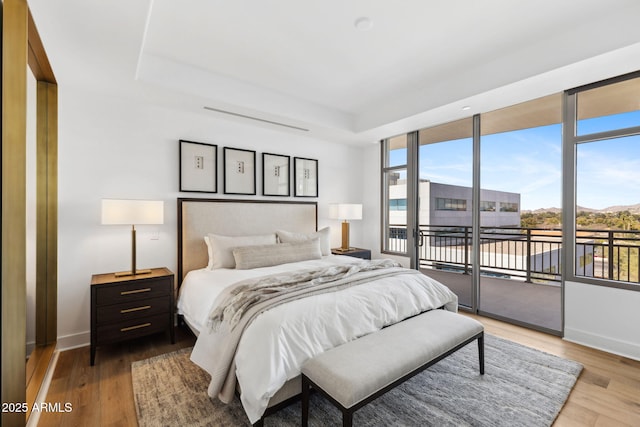 bedroom featuring baseboards, a raised ceiling, wood finished floors, and access to exterior