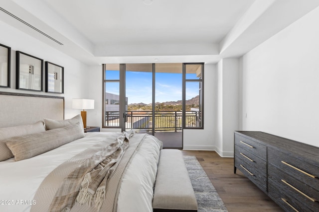 bedroom with a tray ceiling, dark wood-type flooring, a wall of windows, access to outside, and baseboards