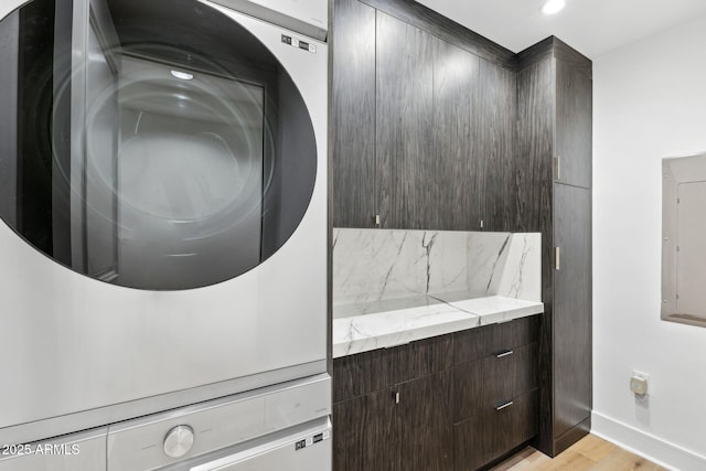 washroom featuring stacked washer / drying machine, recessed lighting, light wood-type flooring, electric panel, and baseboards