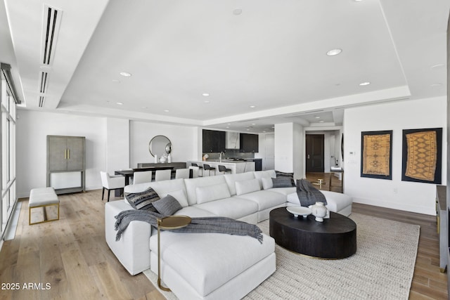 living area with baseboards, light wood finished floors, a raised ceiling, and recessed lighting