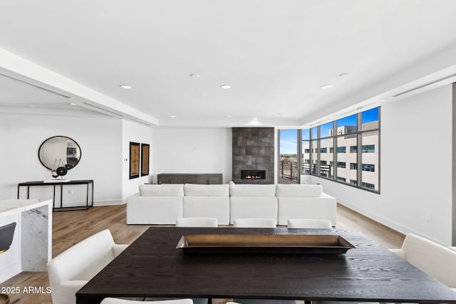 living room featuring light wood-type flooring, a large fireplace, baseboards, and recessed lighting