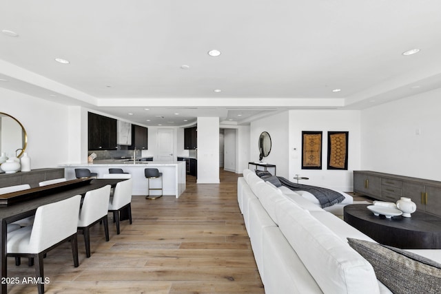 living room with light wood-type flooring, a tray ceiling, and recessed lighting