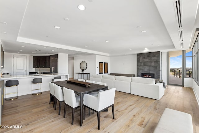 dining space with light wood-type flooring, a fireplace, a wall of windows, and recessed lighting