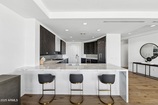 kitchen featuring a breakfast bar area, backsplash, light wood-style floors, a sink, and a peninsula