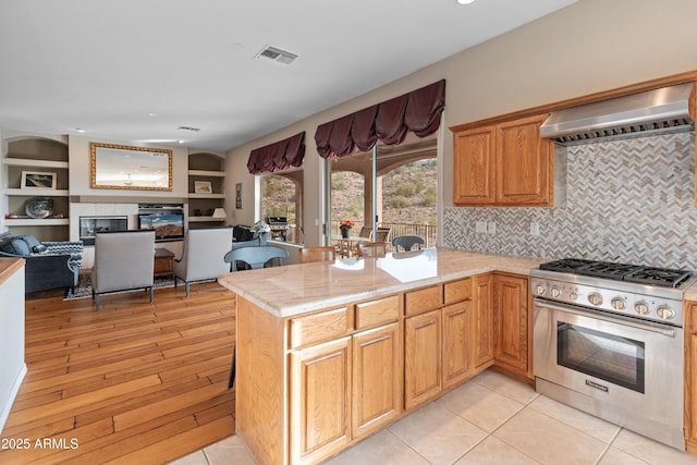 kitchen with kitchen peninsula, premium range hood, high end stainless steel range oven, and a tiled fireplace