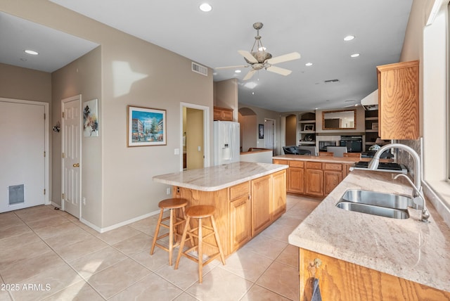 kitchen featuring light stone countertops, sink, white fridge with ice dispenser, light tile patterned floors, and a kitchen island