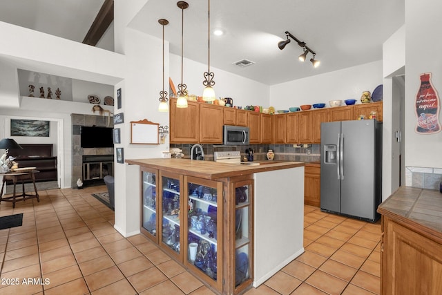 kitchen with backsplash, light tile patterned flooring, decorative light fixtures, a tiled fireplace, and stainless steel appliances