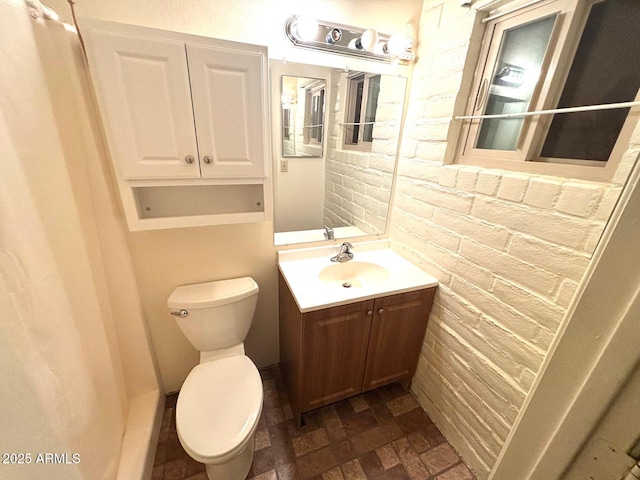 bathroom featuring toilet, vanity, and brick wall