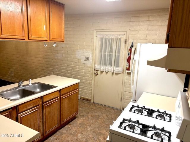 kitchen featuring white appliances, brick wall, light countertops, and a sink