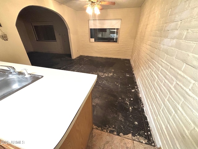 kitchen featuring arched walkways, light countertops, ceiling fan, and brick wall