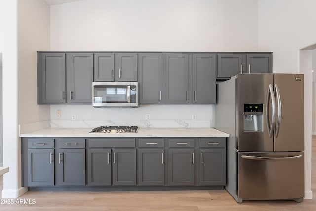 kitchen featuring gray cabinetry, stainless steel appliances, light wood-style floors, and light stone counters