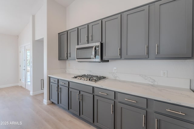 kitchen featuring gray cabinetry, stainless steel appliances, light wood finished floors, and light stone counters