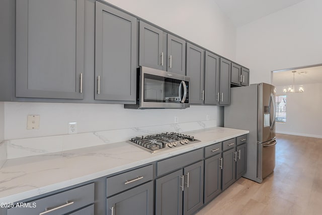 kitchen with light stone counters, appliances with stainless steel finishes, a chandelier, gray cabinetry, and light wood-type flooring