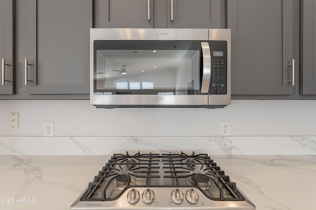 interior details featuring appliances with stainless steel finishes, tasteful backsplash, light stone counters, and gray cabinetry