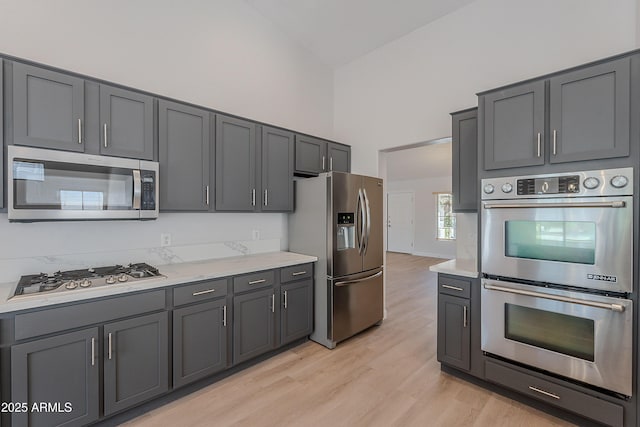 kitchen featuring light wood finished floors, a high ceiling, appliances with stainless steel finishes, and light countertops