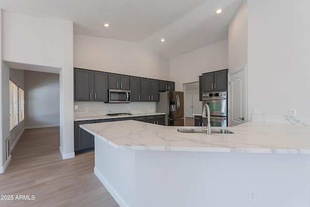 kitchen featuring light stone counters, stainless steel appliances, light wood finished floors, a sink, and a peninsula