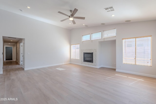 unfurnished living room featuring visible vents, baseboards, a glass covered fireplace, a ceiling fan, and high vaulted ceiling